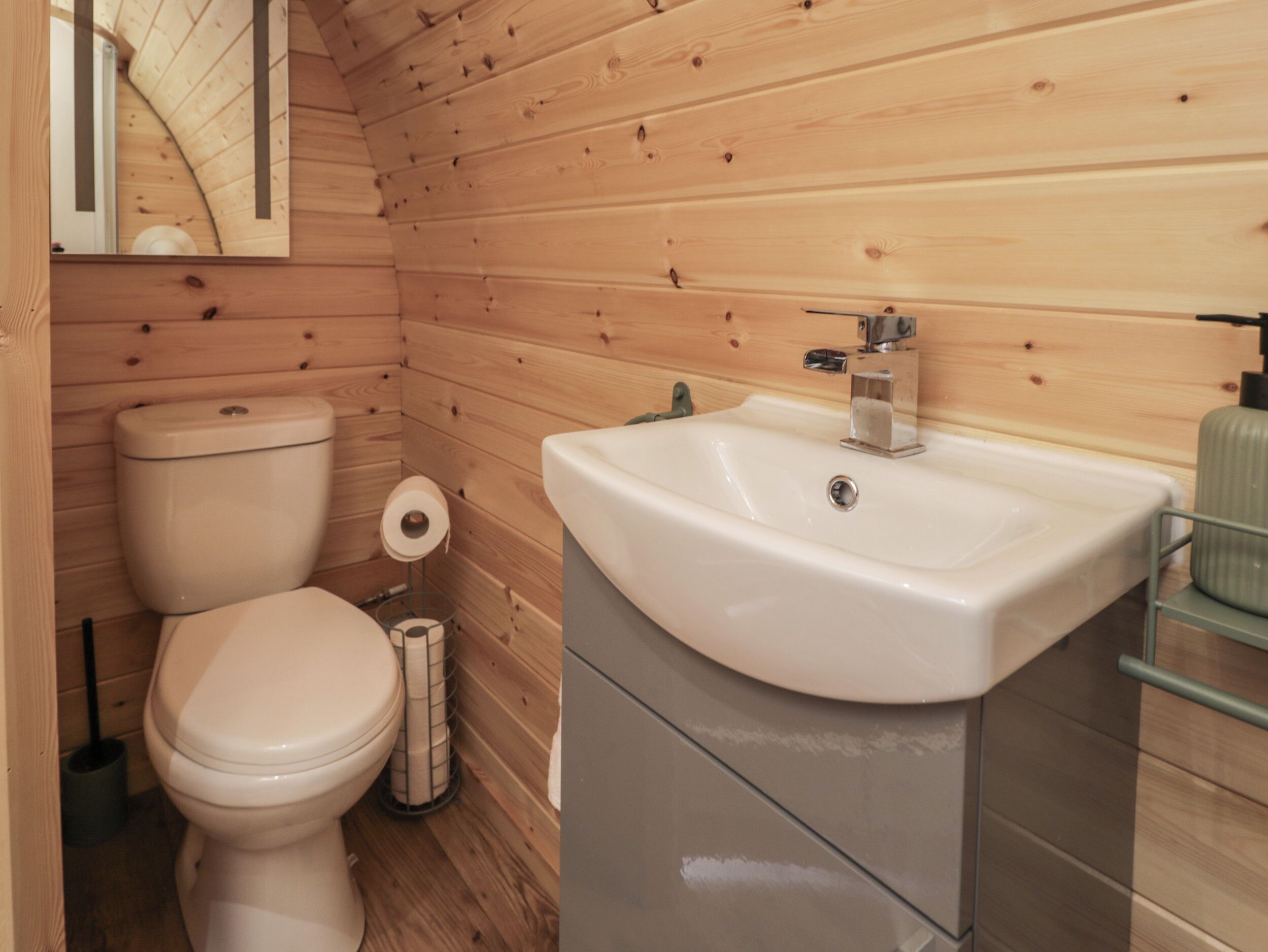 A wooden-paneled bathroom with a toilet, sink, and mirror.