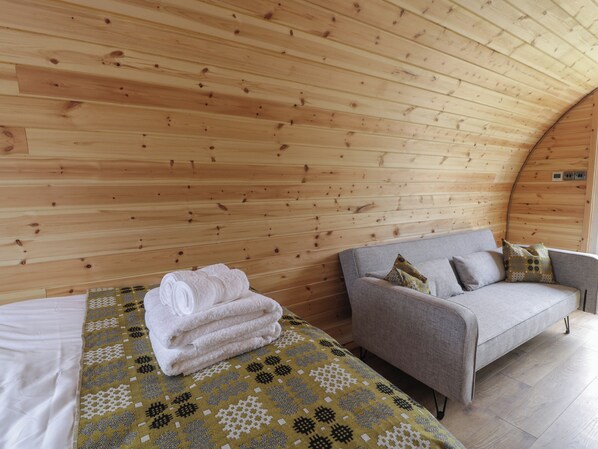 A cozy room with wooden walls, a bed with a patterned blanket, and a grey sofa with pillows. - Dysynni Pod (Tywyn)