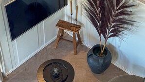 Un accogliente soggiorno con una TV a schermo piatto, un piccolo sgabello di legno, un tavolino rotondo con piano in vetro e un'ampia pianta in vaso.