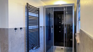 Un bagno moderno con box doccia in vetro, portasciuga e una piccola pianta.