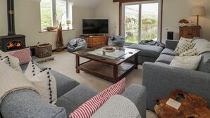 A cozy living room with a fireplace, comfortable seating, and a television. - Pennant Tigi Uchaf (Machynlleth)