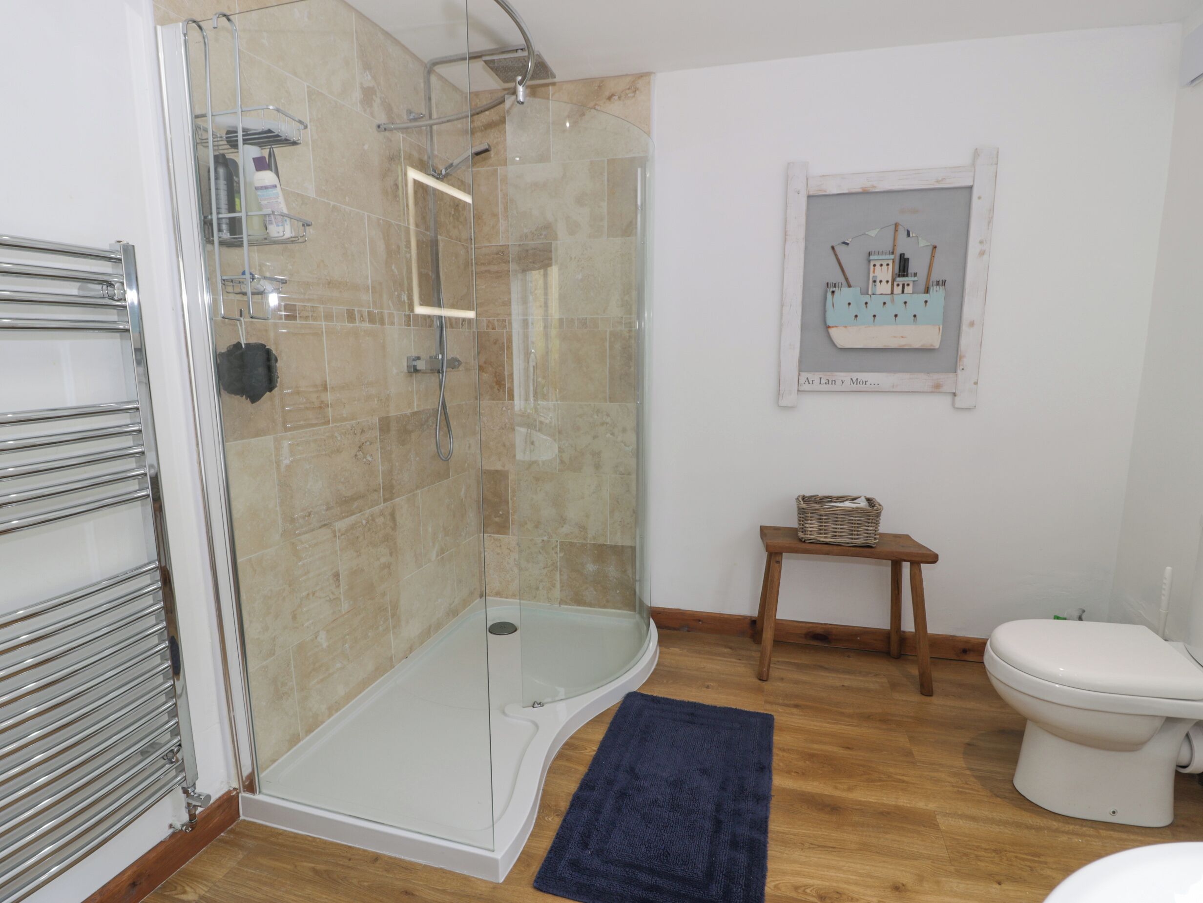A modern bathroom with a glass shower enclosure, a white toilet, and a wooden bench.