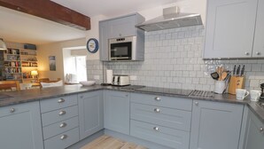 A modern kitchen with grey cabinets, a microwave, and a toaster. There is a wooden floor and a bookshelf in the background. - Pennant Tigi Uchaf (Machynlleth)