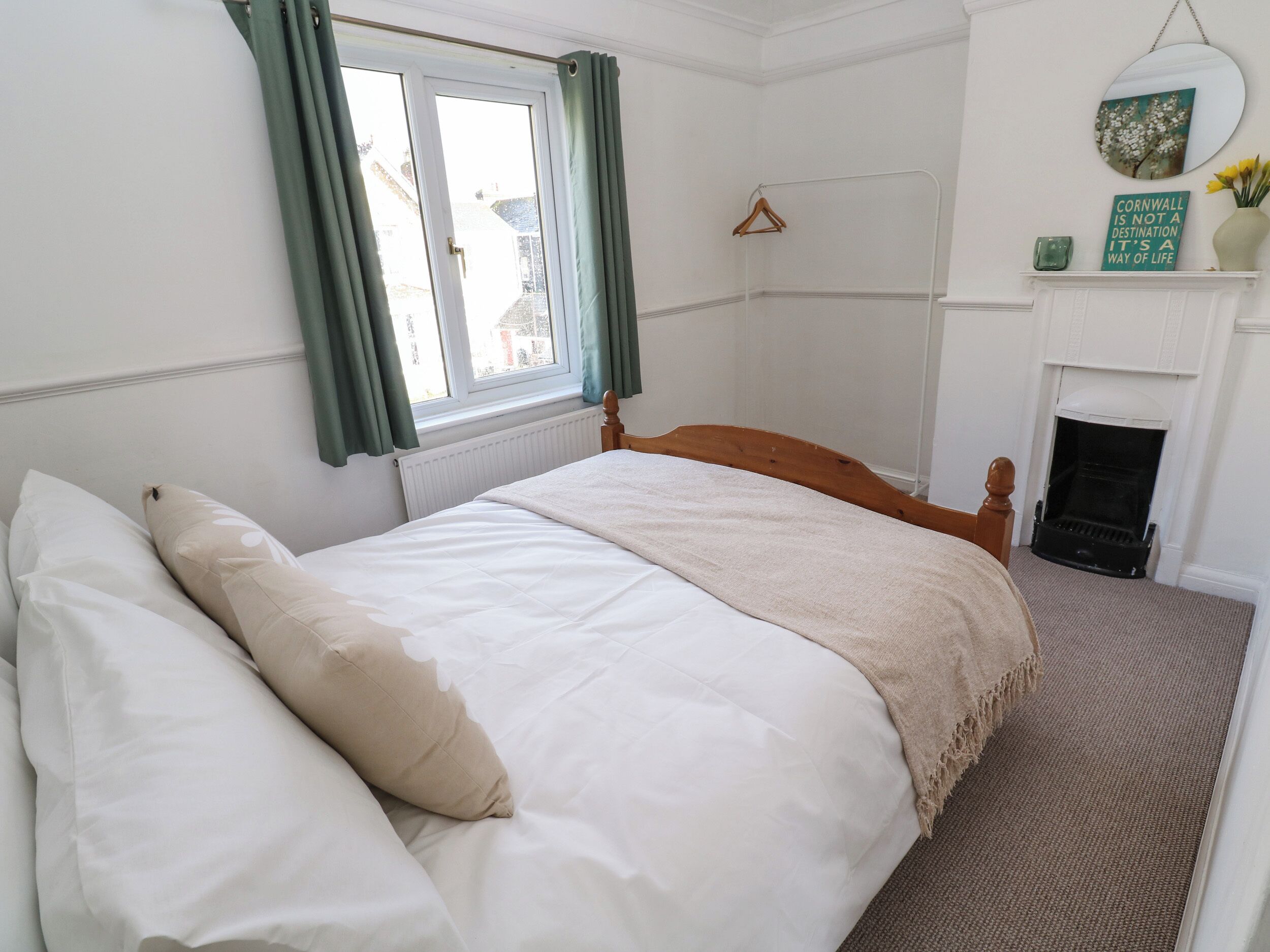 A neatly made bed with white and beige bedding, a wooden headboard, and a window with green curtains.