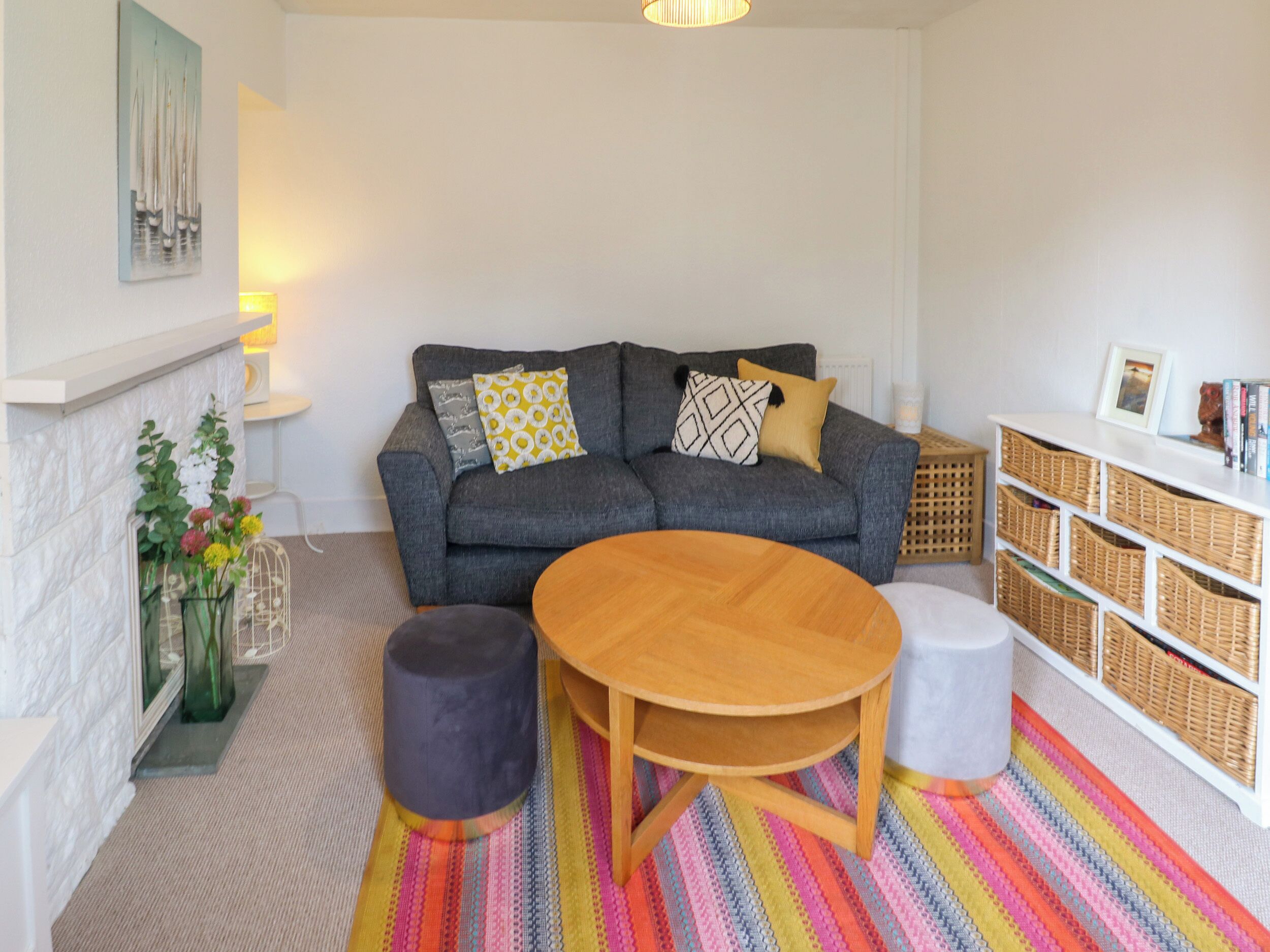 A cozy living room with a grey sofa, a wooden coffee table, and a colorful striped rug.
