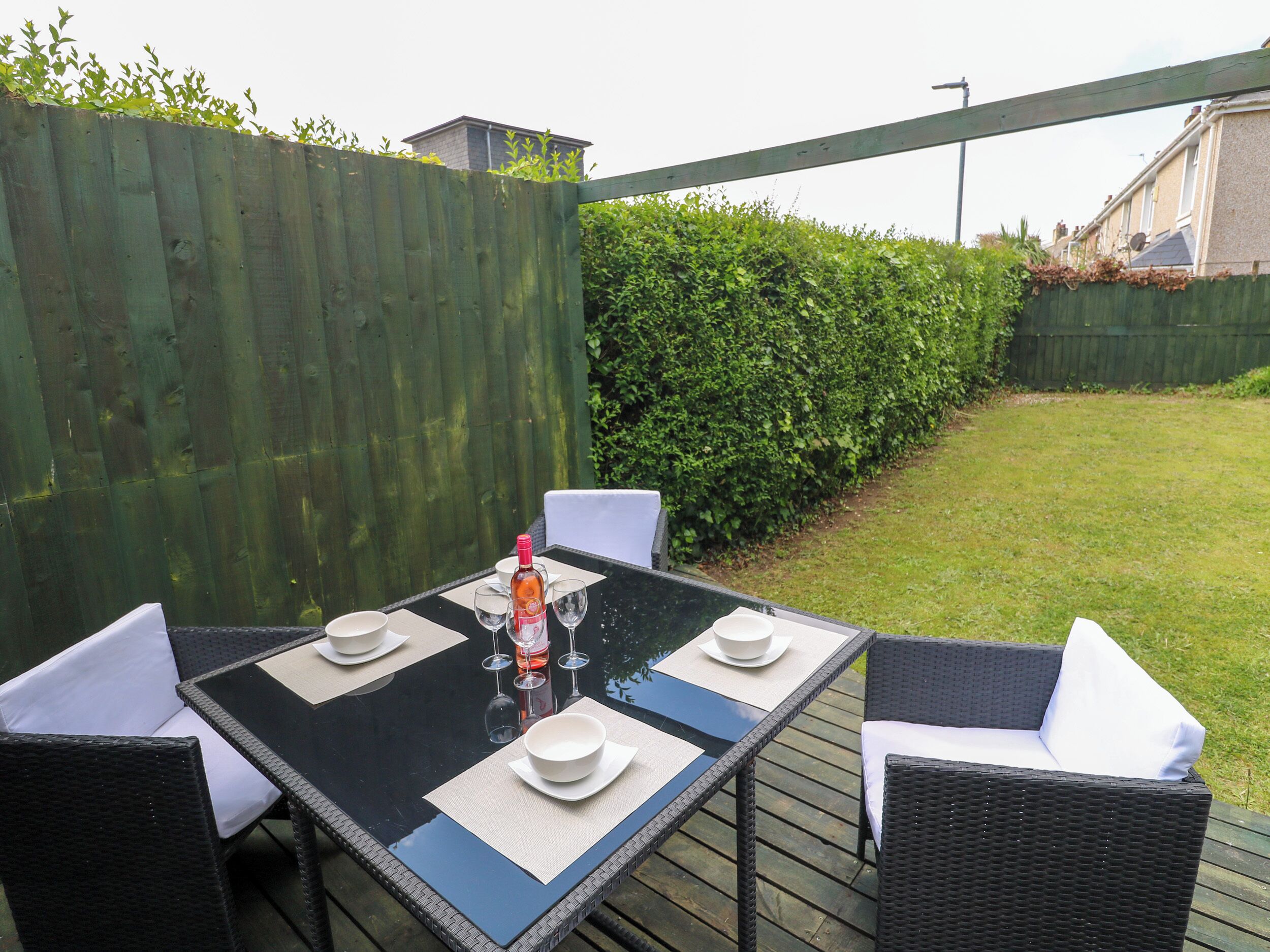 An outdoor dining area with a table set for four, surrounded by wicker chairs with white cushions.