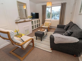 A living room with a sofa, armchair, television, and a window with curtains.