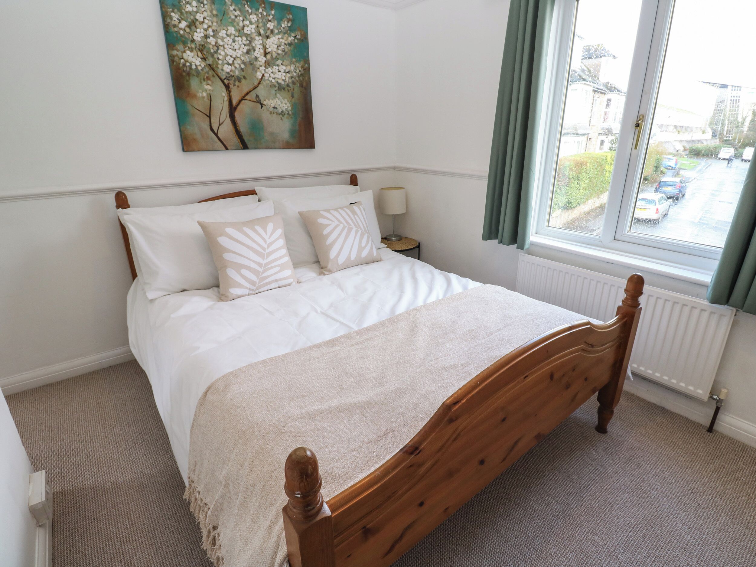 A neatly made bed with a wooden headboard, a bedside table with a lamp, and a window with curtains.