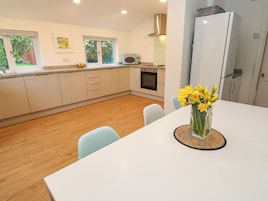 A modern kitchen with white cabinets, a built-in oven, and a microwave. There is a dining table with chairs and a vase of flowers.