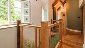 Una escalera de madera con barandillas de vidrio, vistas al verdor exterior y una lámpara moderna.