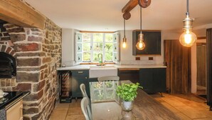 Una cocina con pared de piedra, vigas de madera, horno empotrado y ventana con vistas al verdor.