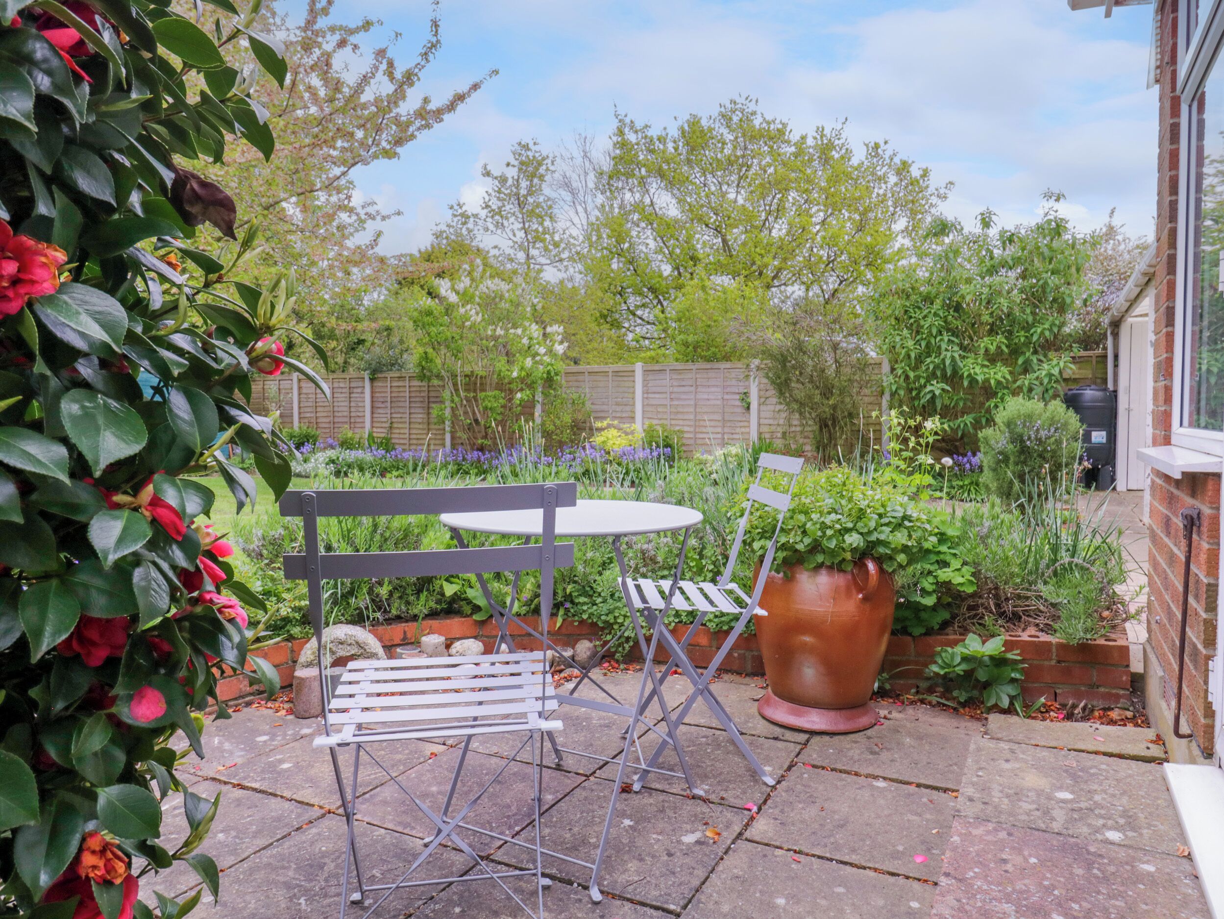 A patio with a metal table and chairs, surrounded by lush greenery and a brick wall.