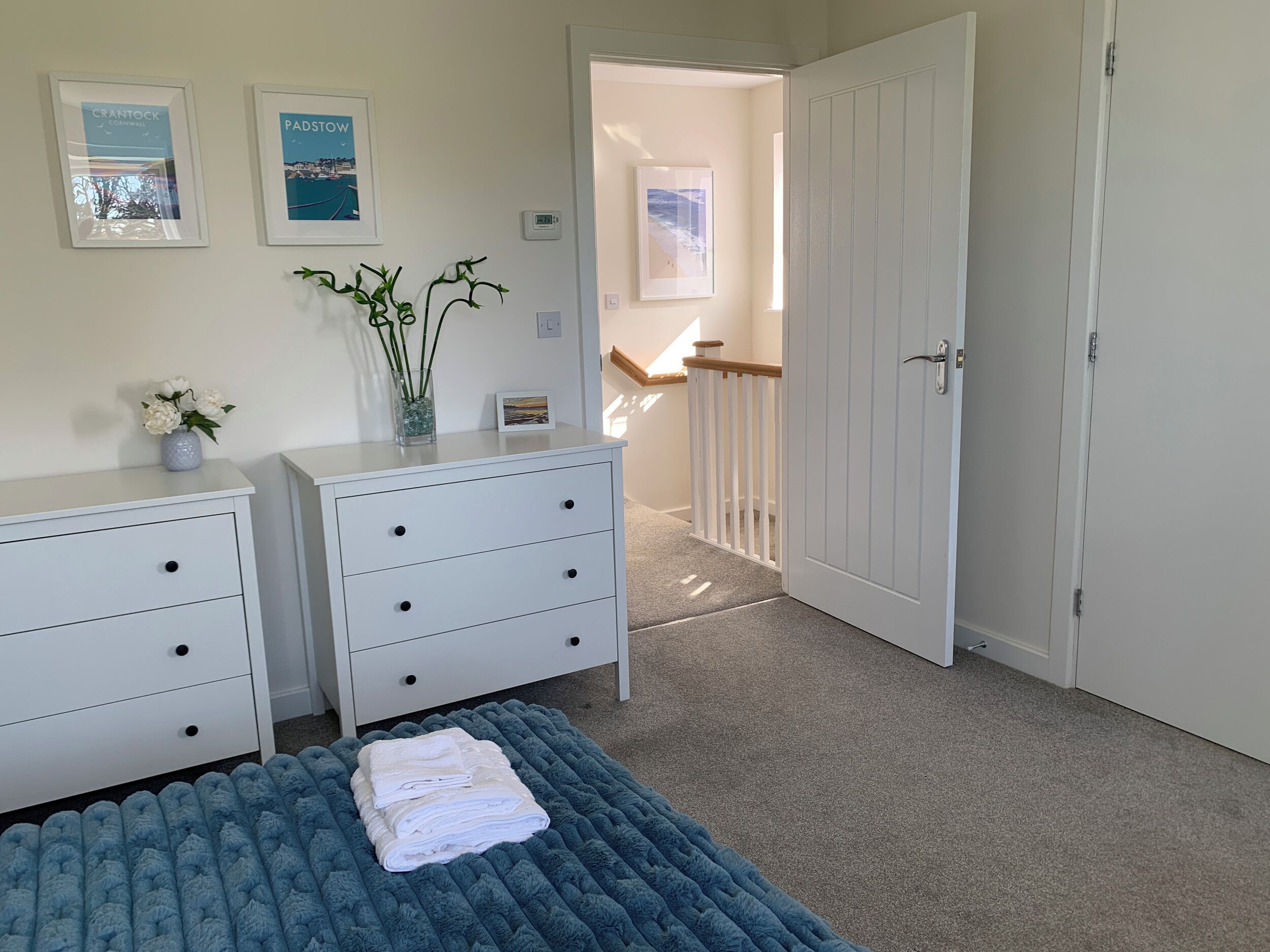 Une chambre à coucher avec un lit, une commode, un vase de fleurs et deux tableaux encadrés accrochés au mur.