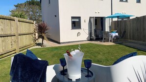 A modern house with a patio area featuring a table with drinks and a blue umbrella. - 2 Boathouse Terrace (Wadebridge)