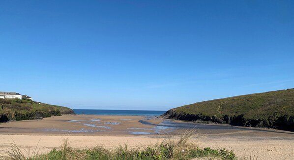 A coastal landscape with a sandy beach, grassy hills, and a clear blue sky. - 2 Boathouse Terrace (Wadebridge)