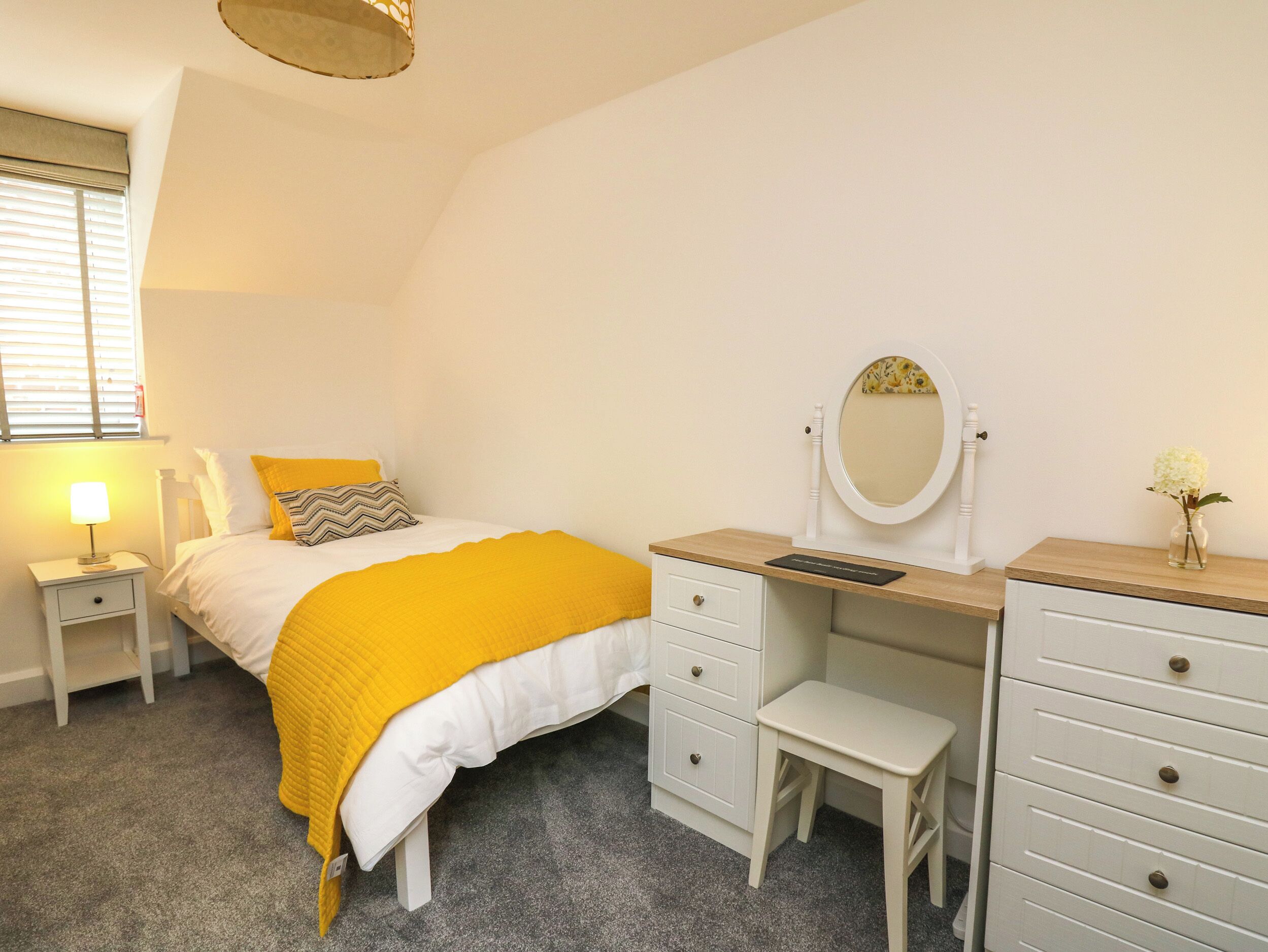 A bedroom with a bed, a nightstand, a dresser, a mirror, and a small stool.