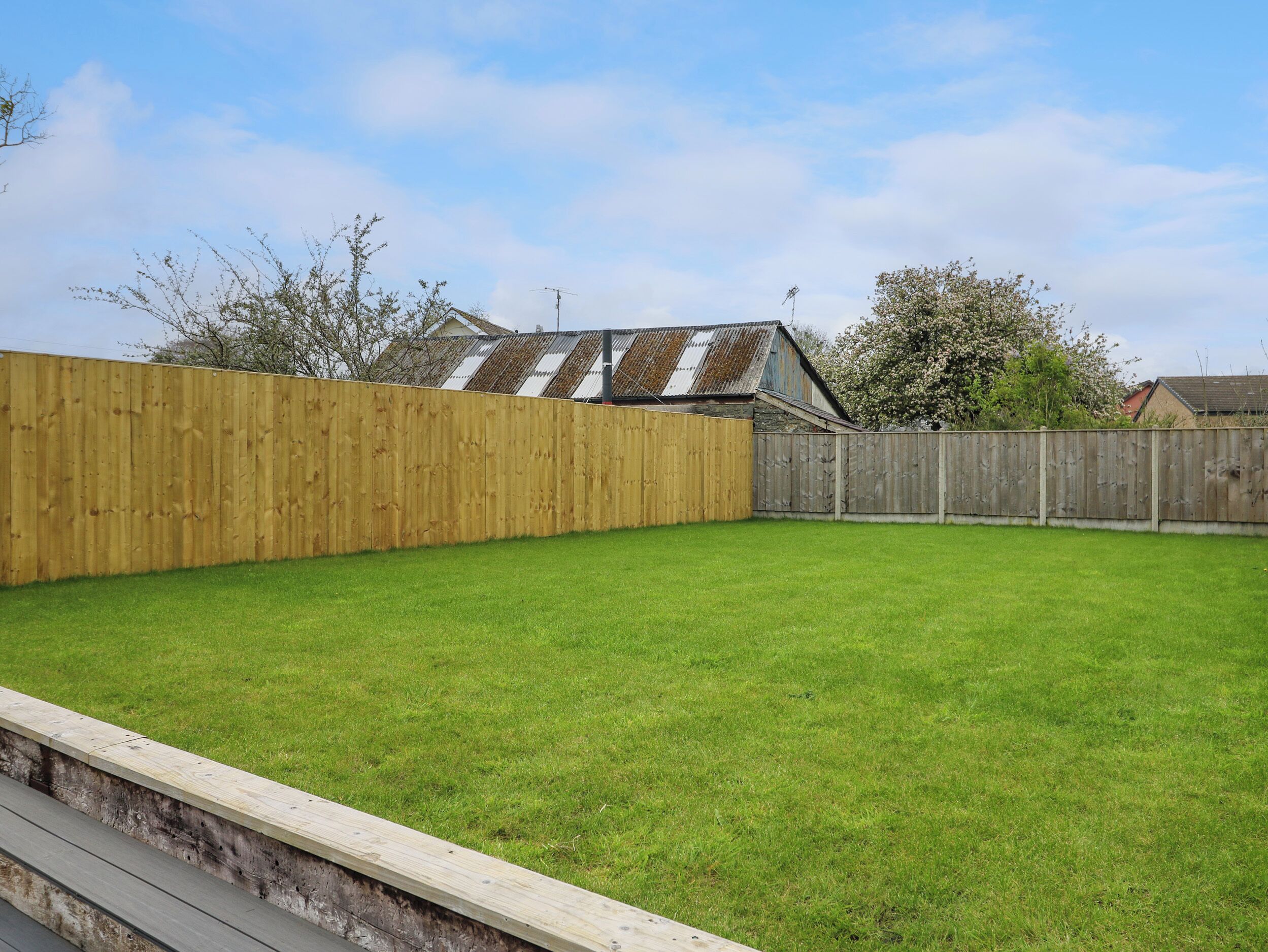 A backyard with a wooden fence, a grassy lawn, and a house with a metal roof in the background.