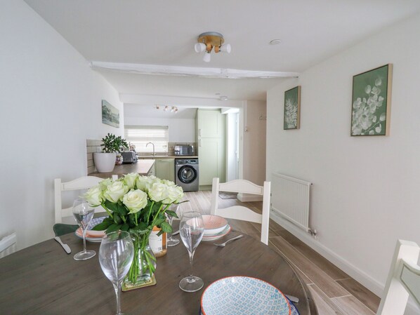 A dining area with a table set for two, a vase with flowers, and a view into the kitchen. - 2 Penporth (Rhayader)