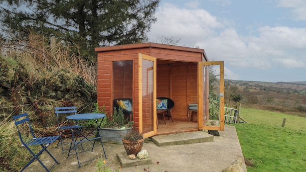 Eine Holzhütte mit Glastür, Tisch und Stühlen vor der Tür.