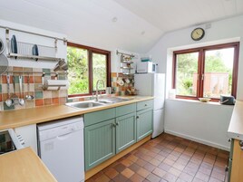 A kitchen with a Bosch dishwasher, a sink, green cabinets, and a window with a view of greenery.