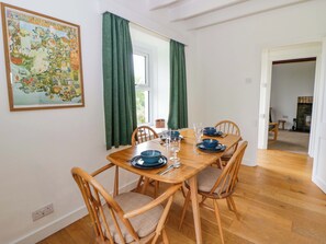 Un coin repas avec une table en bois dressée pour quatre personnes, des rideaux verts et une carte colorée accrochée au mur.