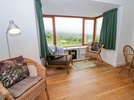 A cozy room with a view of the countryside, featuring wicker furniture, a desk, and a lamp.