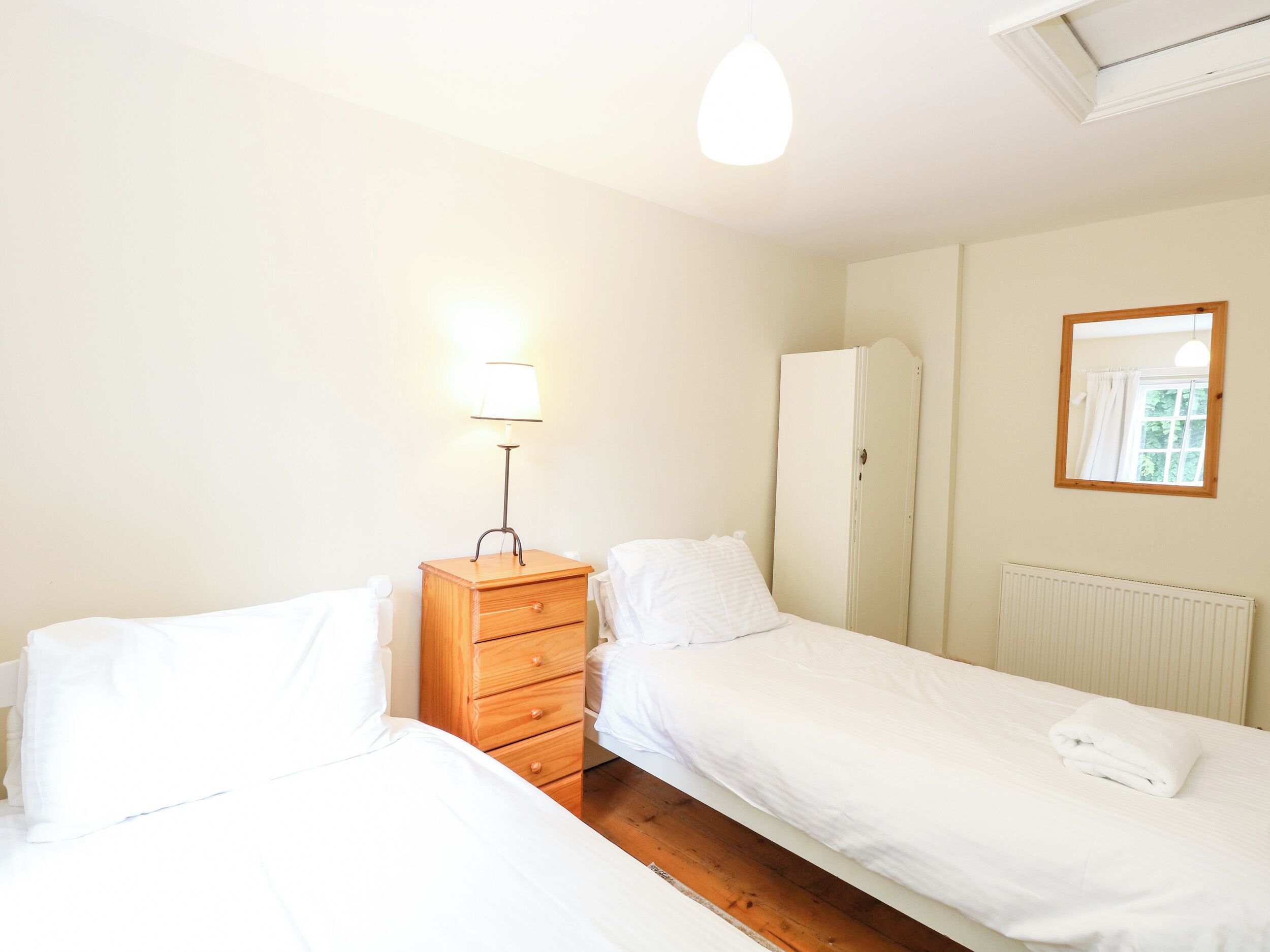 Ein Schlafzimmer mit zwei Betten, einer Holzkommode, einer Lampe, einem Kleiderschrank und einer Heizung.
