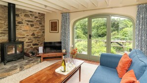 Un salon chaleureux avec une cheminée en pierre, un téléviseur, un canapé et une grande fenêtre donnant sur un paysage verdoyant.
