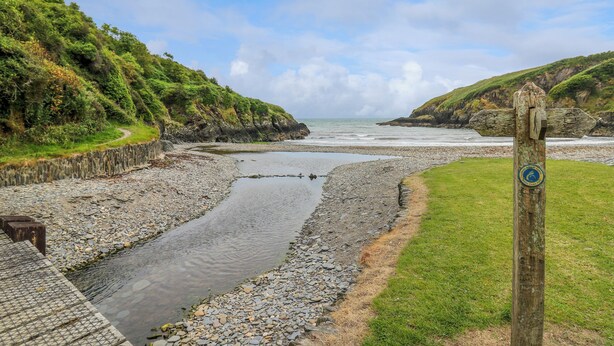 Un paysage côtier avec une plage rocheuse, un étroit chenal et un panneau indicateur en bois.