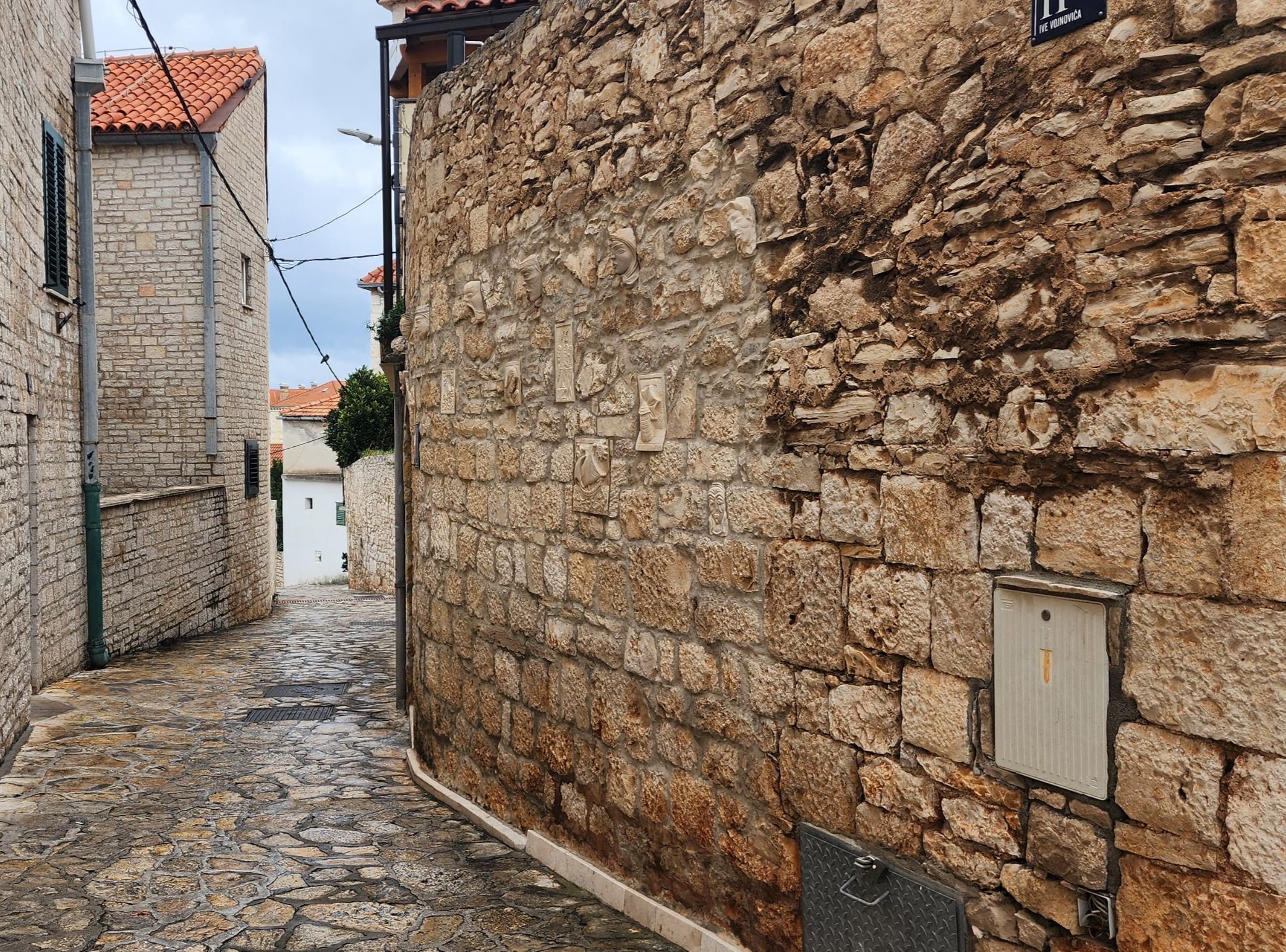 A narrow stone-paved street flanked by buildings with stone walls and tiled roofs.