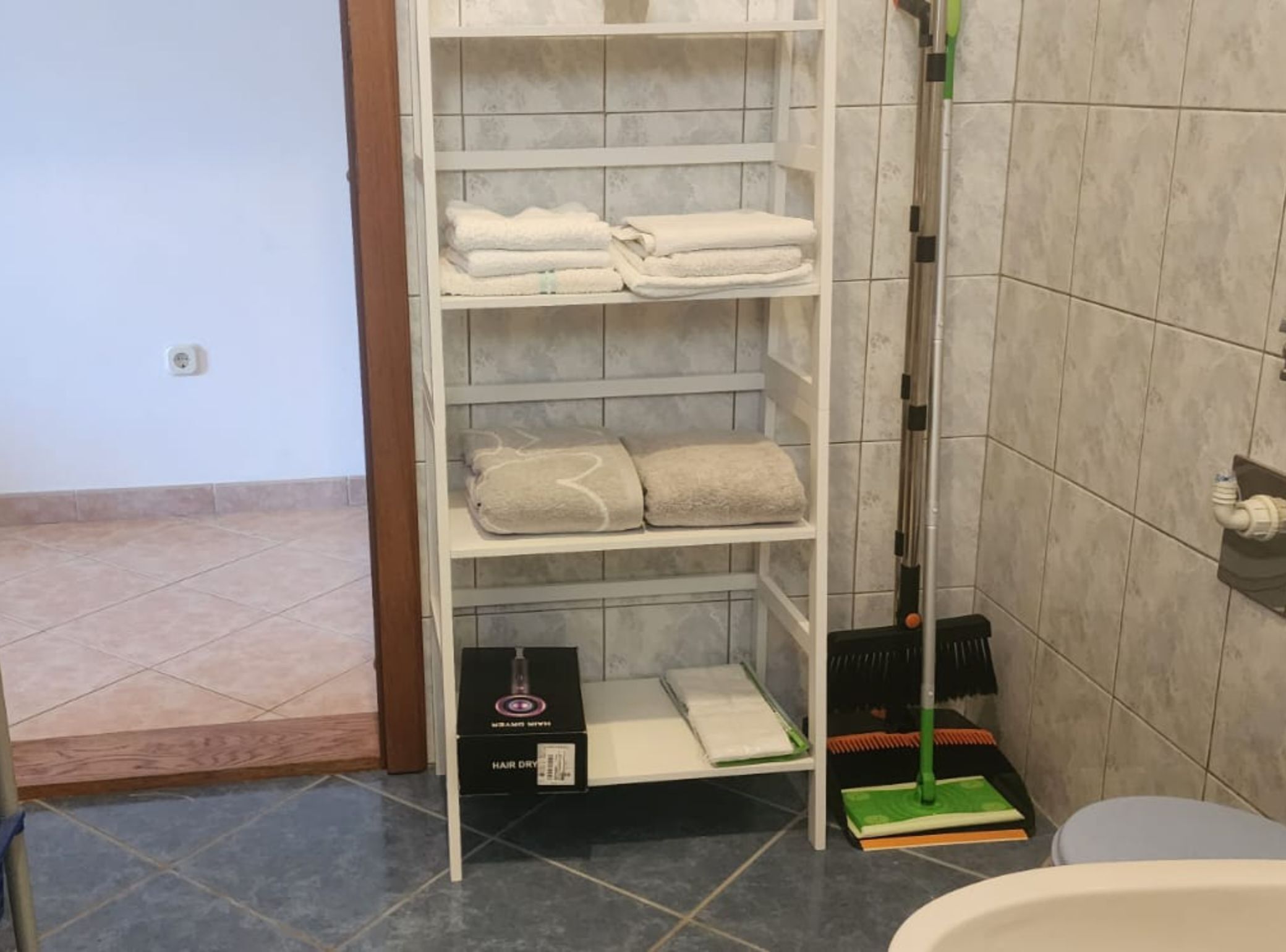 A bathroom with a white shelf holding towels, a hairdryer, and a broom.