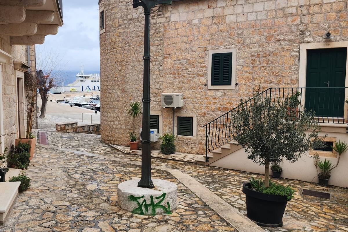 A stone building with a staircase leading to a door, surrounded by potted plants and a cobblestone street.