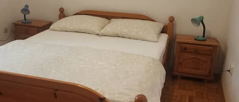A wooden bed with a white bedspread and two pillows, flanked by two wooden nightstands with lamps.