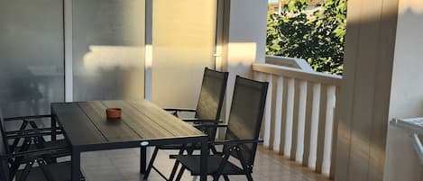 Un balcon avec une table et des chaises, une porte-fenêtre coulissante et une vue sur la verdure et les bâtiments.
