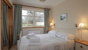 A neatly made bed with a floral bedspread, a bedside lamp, and a window with curtains. - Tigh na Drochit (Kyle)