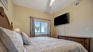 Ein Schlafzimmer mit einem Bett, einem an der Wand montierten Fernseher, einem Fenster mit Vorhängen und einem Deckenventilator.