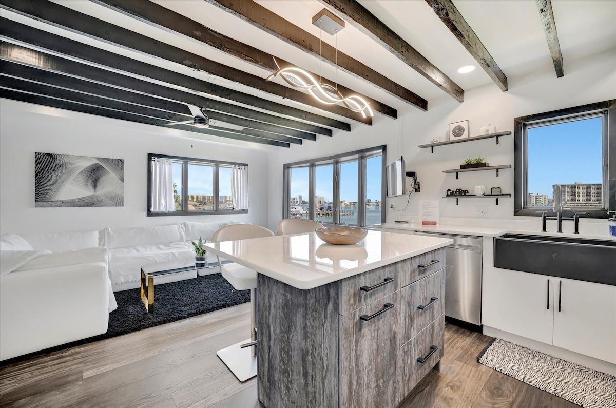 Un intérieur moderne avec un îlot de cuisine, des meubles blancs et de grandes fenêtres offrant une vue sur la ville.