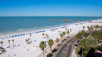 Pristine white sands meet crystal-clear turquoise waters along this stunning Gulf Coast beach, framed by swaying palms and a historic fishing pier extending into the calm sea.