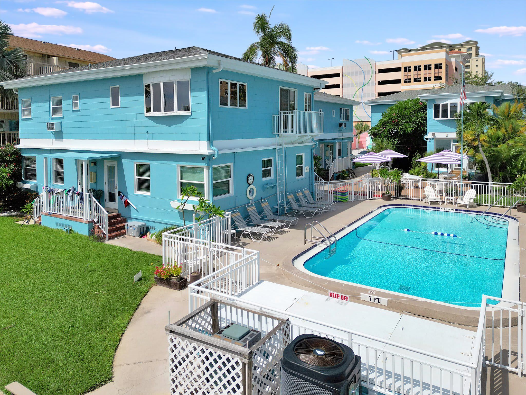 This charming turquoise beach house features a spacious backyard with a sparkling pool, perfect for sunny days. The lush green lawn and tropical palms frame your private outdoor retreat.