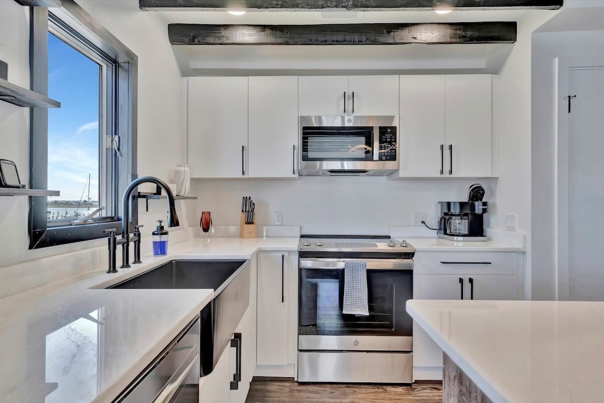 Step into your bright, modern kitchen with sleek white cabinetry and contemporary appliances, where morning coffee moments are framed by waterfront views through large windows.