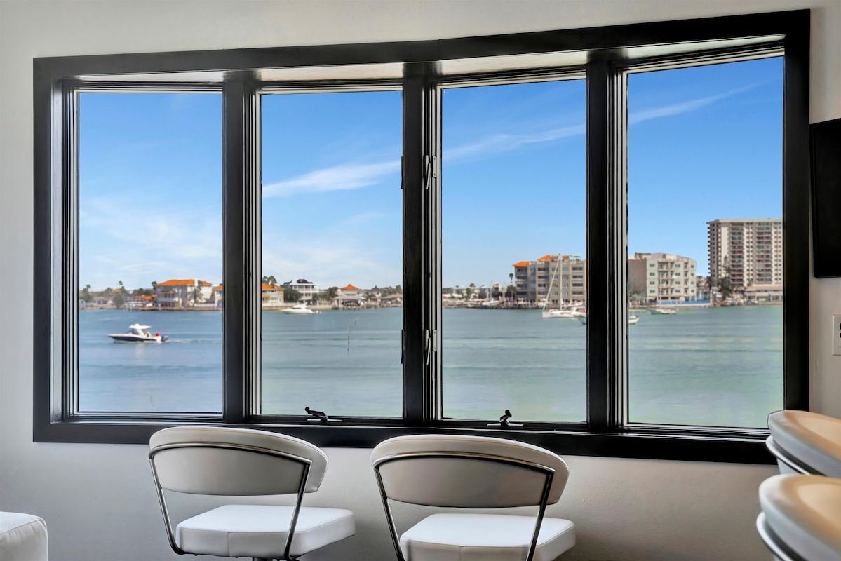 Settle into your waterfront sanctuary and gaze out at tranquil bay waters dotted with boats, framed by a coastal cityscape. This serene perch invites you to sip morning coffee while soaking in the calming blue hues.