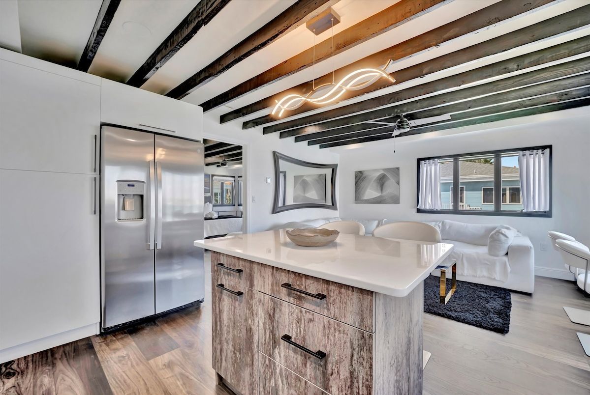 Gather around the sleek kitchen island under dramatic exposed beams, where modern design meets warm wood accents. Your open-concept retreat flows seamlessly into a bright living space, perfect for entertaining or simply unwinding in style.