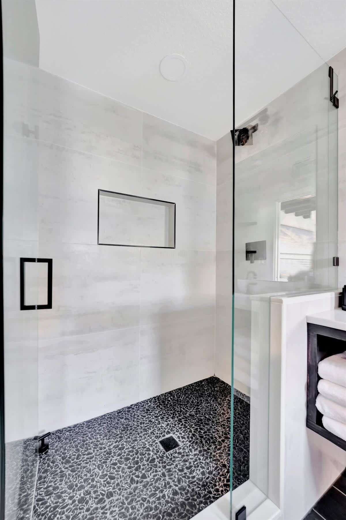 A modern bathroom with a glass shower enclosure, a marble floor, and a minimalist design.