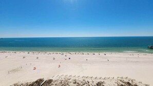 A beach with a clear sky, calm sea, and a sandy shore with umbrellas and beachgoers. - Beachfront Views Admirals Quarters Pools Sleeps 6 (Orange Beach)