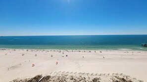 Una playa con cielo despejado, mar tranquilo y orilla arenosa con sombrillas y gente.