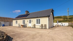 A single-story house with a tiled roof, solar panels, and a patio with outdoor furniture. - Cottage View (Carrigaholt)