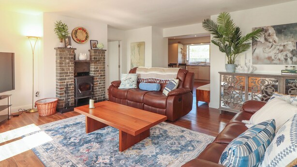 A cozy living room with a leather sofa, a wooden coffee table, and a patterned rug. There is a fireplace with a brick surround, a television, and a basket on the floor. - Cottage View (Carrigaholt)