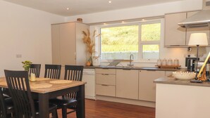A modern kitchen with a dining area, wooden flooring, and a window providing natural light. - Cottage View (Carrigaholt)