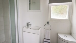 A bathroom with a glass shower enclosure, a white sink with a faucet, a toilet, and a towel hanging on a ring. - Chalet 32 (Aberystwyth)