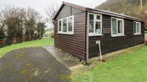 A small, single-story wooden cabin with a sloped roof and white-framed windows. - Chalet 32 (Aberystwyth)